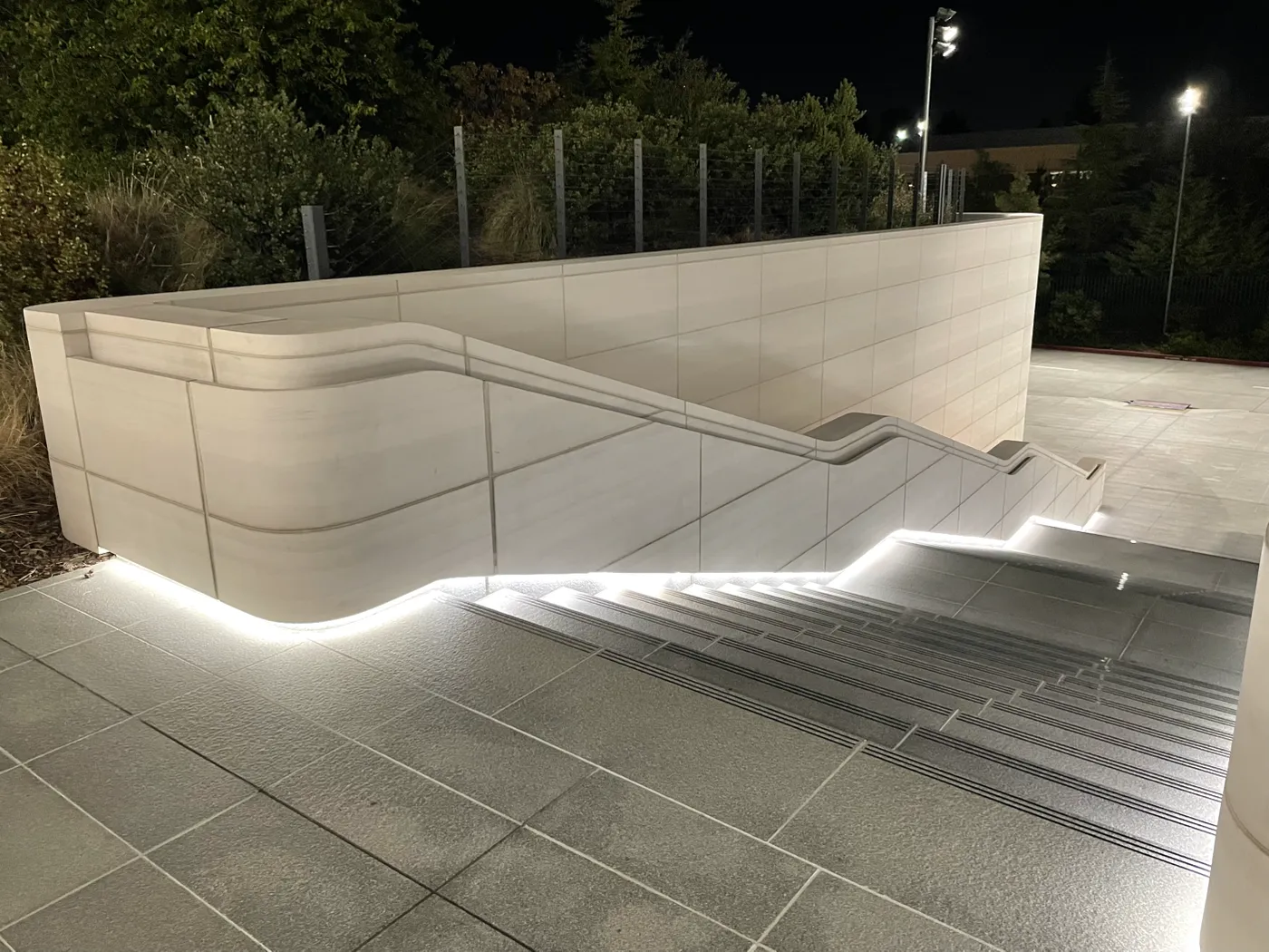 A balustrade wall at night — a continuous sculpted rail moulded into the panel, an LED cove glowing beneath it