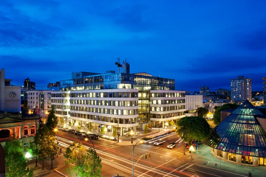 The Atrium at dusk — white UHPC bands sweeping the curved corner of Yates and Blanshard under a glass rooftop