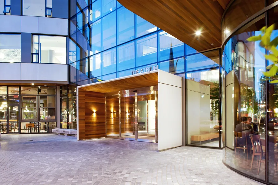 The Atrium's entry — a crisp white precast vestibule surround framing a wood-lined portal beneath the glass facade
