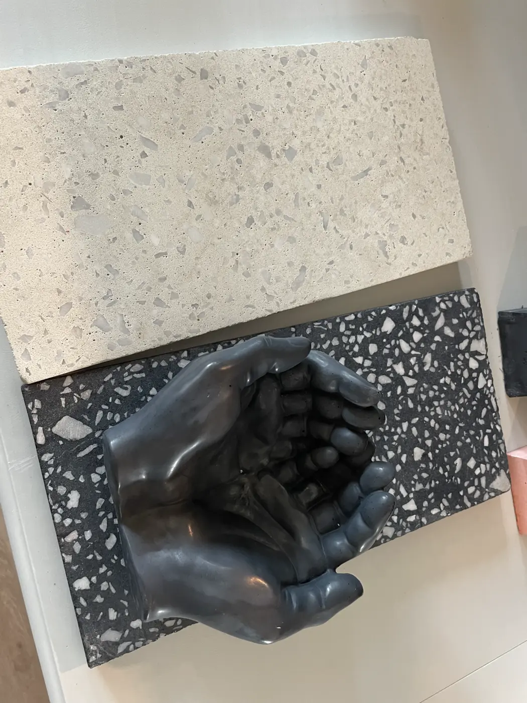 A charcoal cast of cupped hands mounted on a black terrazzo panel beside a white terrazzo slab