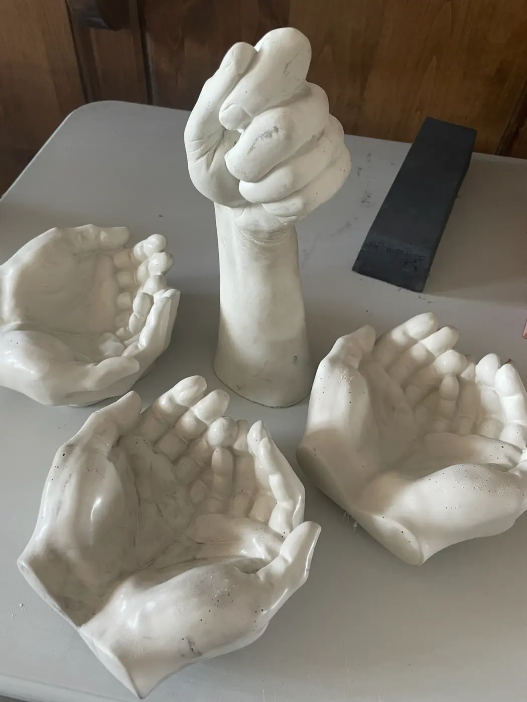 Three white cupped-hand bowl casts and one raised fist on the shop worktable