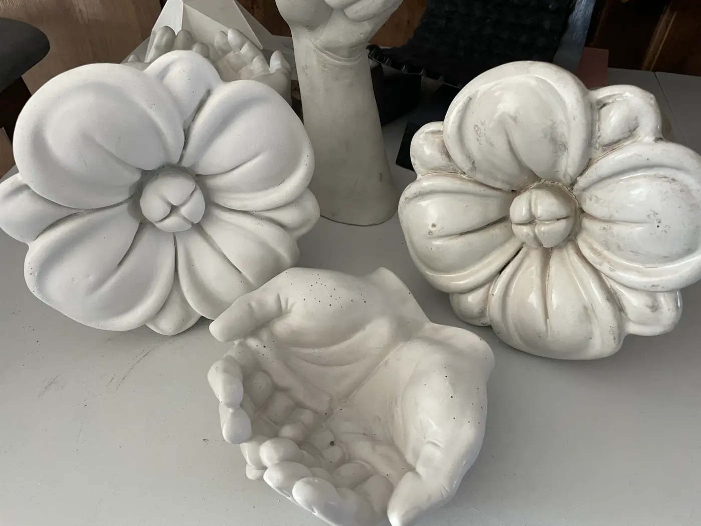 Two large cast flower rosettes side by side — the century-old glazed terracotta original beside the fresh unsealed casting — with cupped-hands casts behind