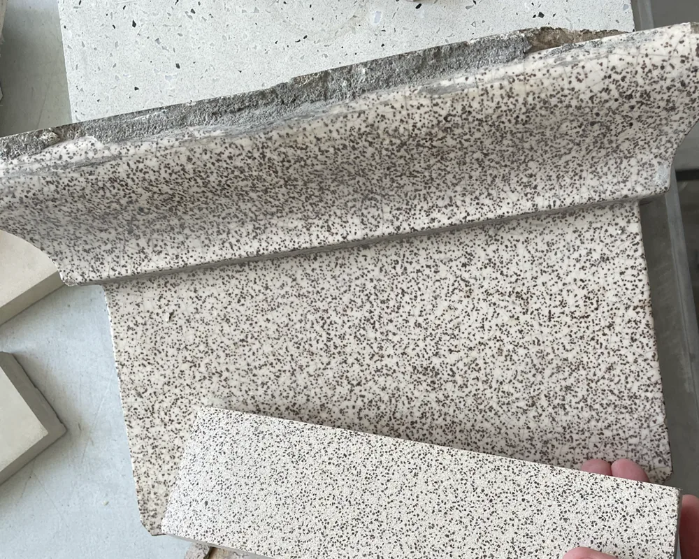 A freshly cast UHPC sample held against an original glazed terracotta block — the speckled tone and fleck pattern match