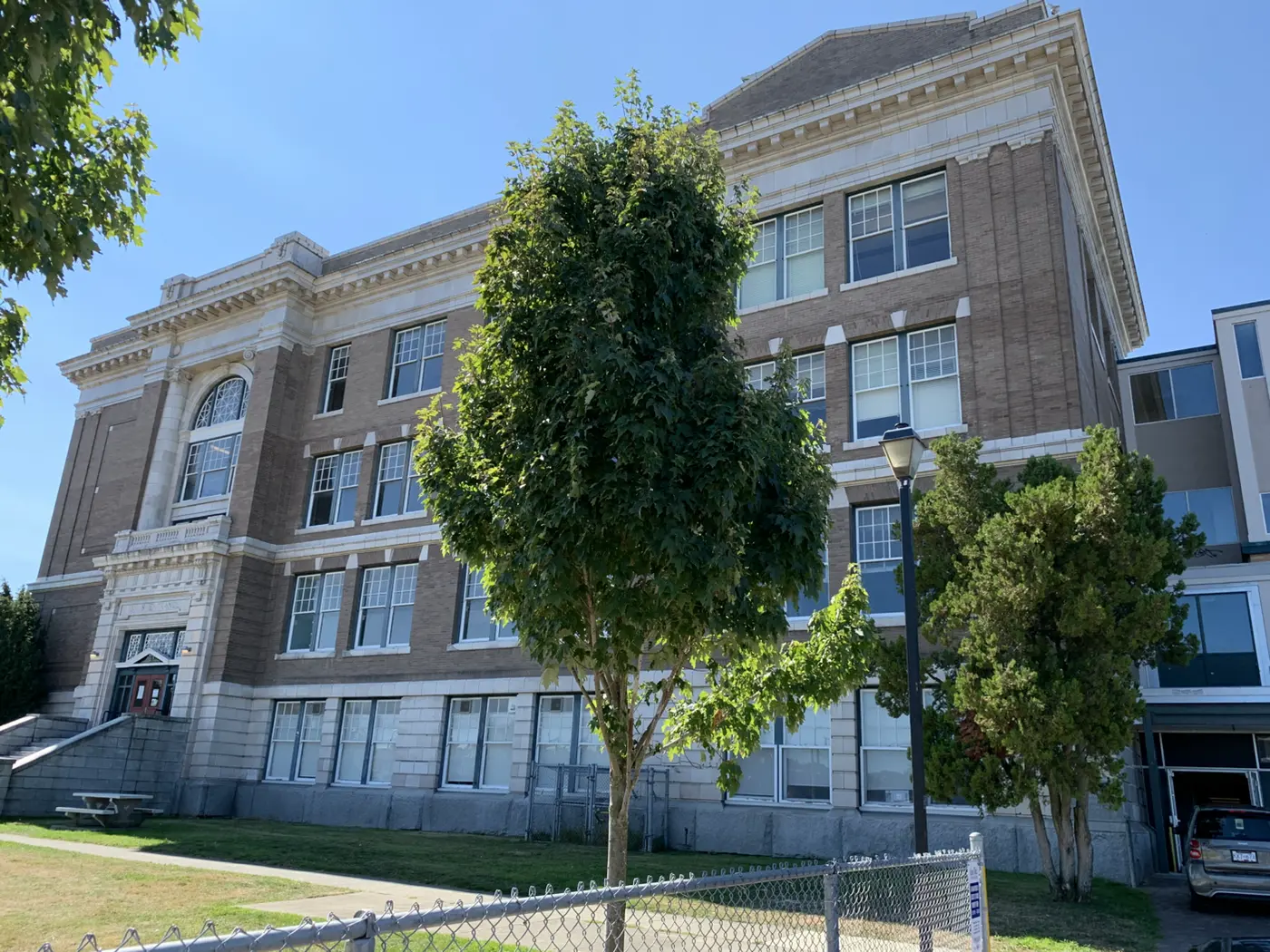 The 1914 Victoria High School in summer sun — full brick and terracotta facade with the modillion cornice Szolyd recast
