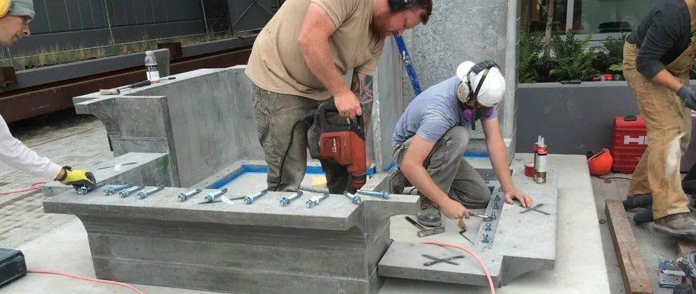 Crew installing the Substation Pavilion base panels, rows of cast-in bolts visible along the UHPC edge