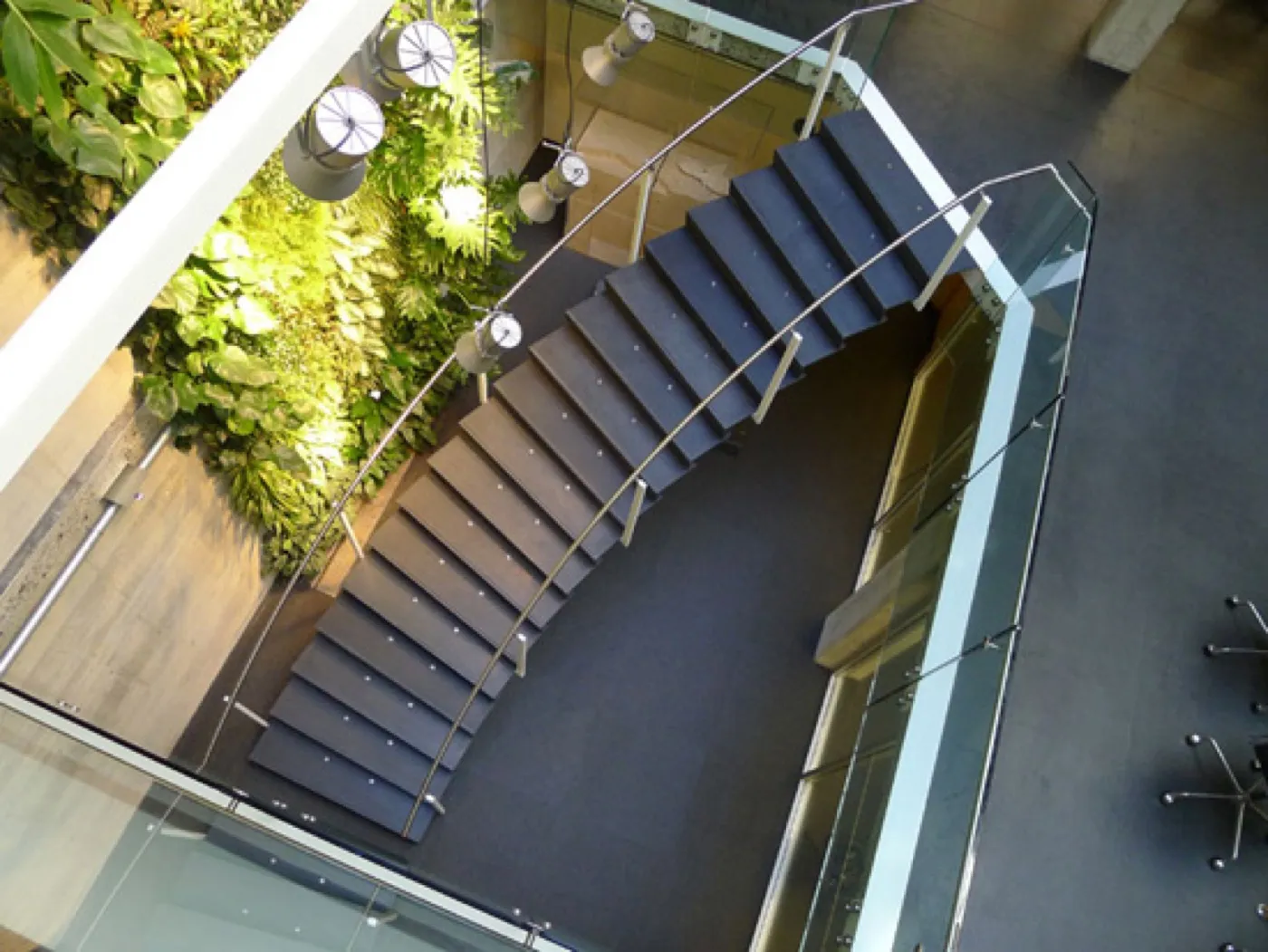 The same flight seen from high above, curving through the atrium past a living wall behind a glass balustrade