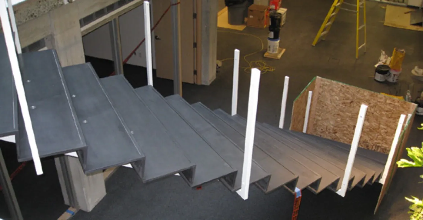 The flight part-installed — L-shaped UHPC tread-and-riser units set on temporary props, guard posts and site clutter around them