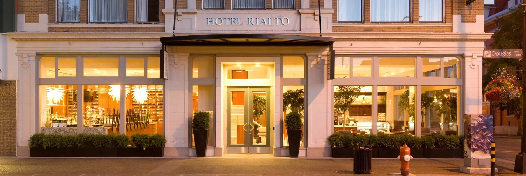 The restored Hotel Rialto facade at dusk — white columns and warm light on Douglas Street, Victoria