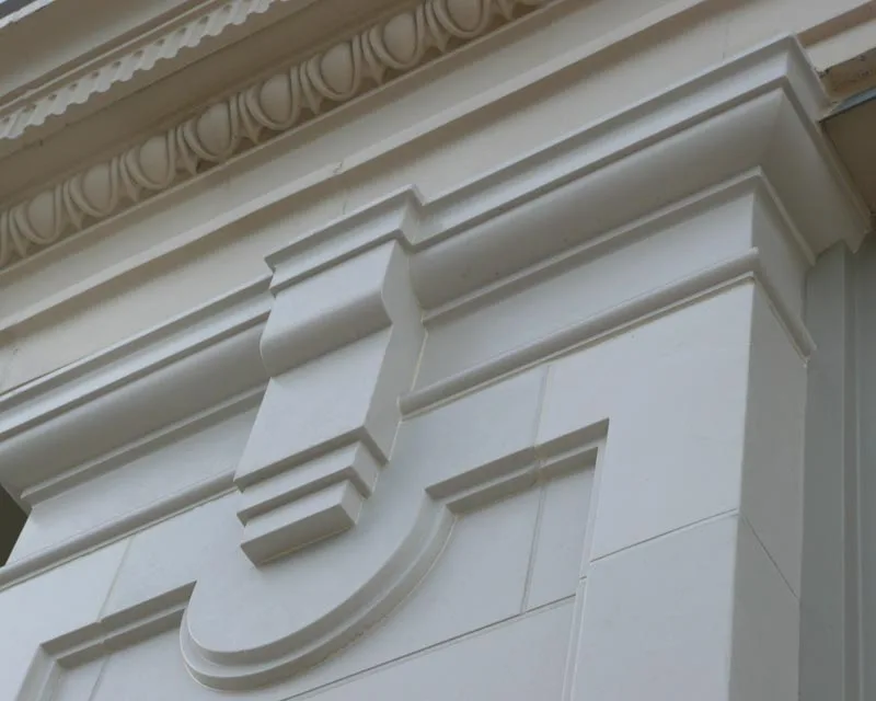 Detail of the finished white cladding — egg-and-dart cornice, console bracket and fine joint lines between cast panels