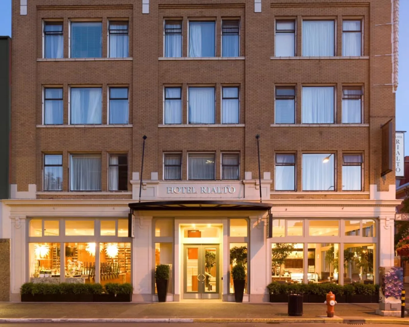 The Hotel Rialto at dusk — the full brick facade above the restored white column line and lit storefronts