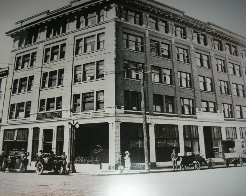 Archival black-and-white photograph of the building in its first life as the Douglas Hotel, with period cars at the kerb