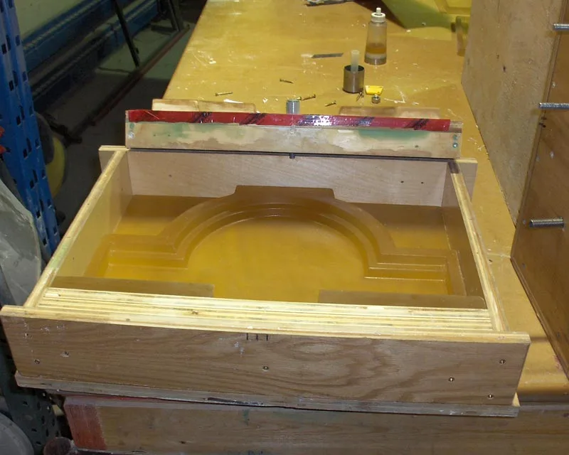 An amber rubber mold of an arched column-capital profile, seated in its plywood crate on the shop bench