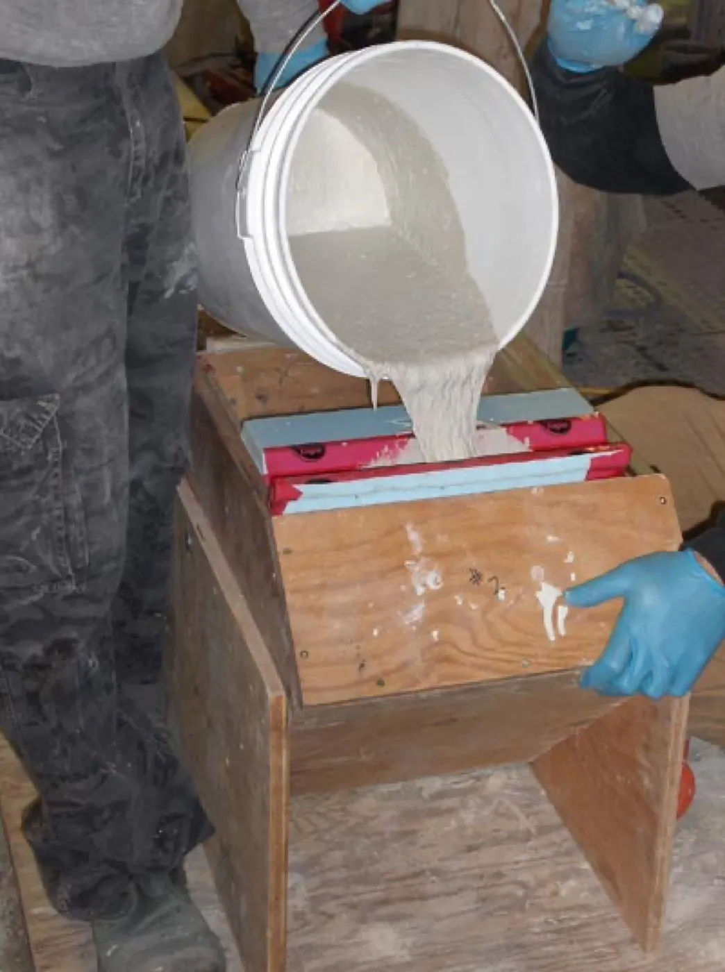 White Ductal poured by hand from a bucket into a small column-profile mold in the shop
