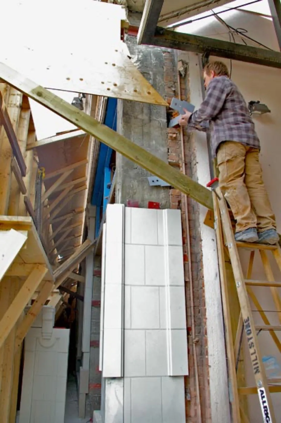 A worker on a ladder setting white UHPC column shells against the stripped column on site