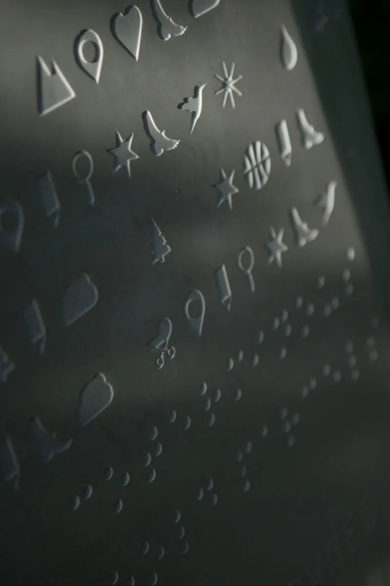 Relief icons and braille cast into a grey Ductal concrete surface, raking light