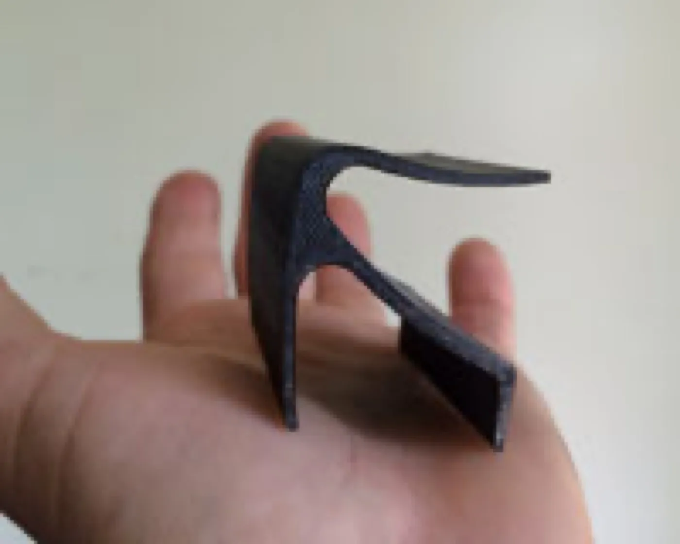A small black 3D-printed model of the Sofi bench held in one hand, its cantilevered seat curving out