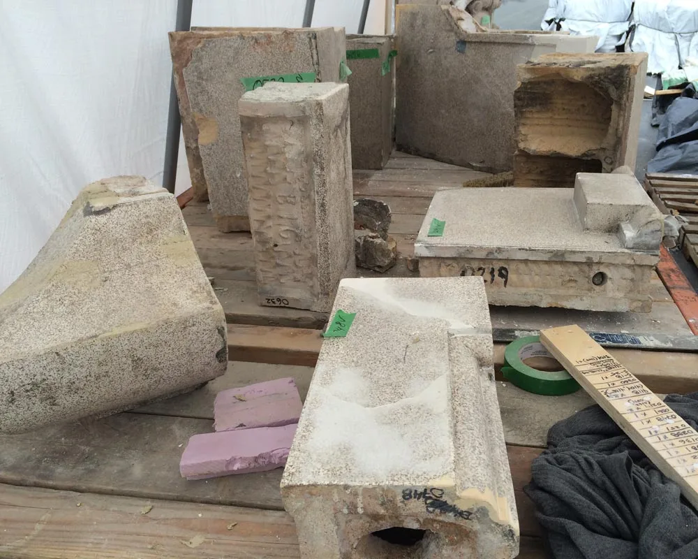 Salvaged original terracotta blocks on pallets under a site tent, each tagged and chalk-numbered for cataloguing