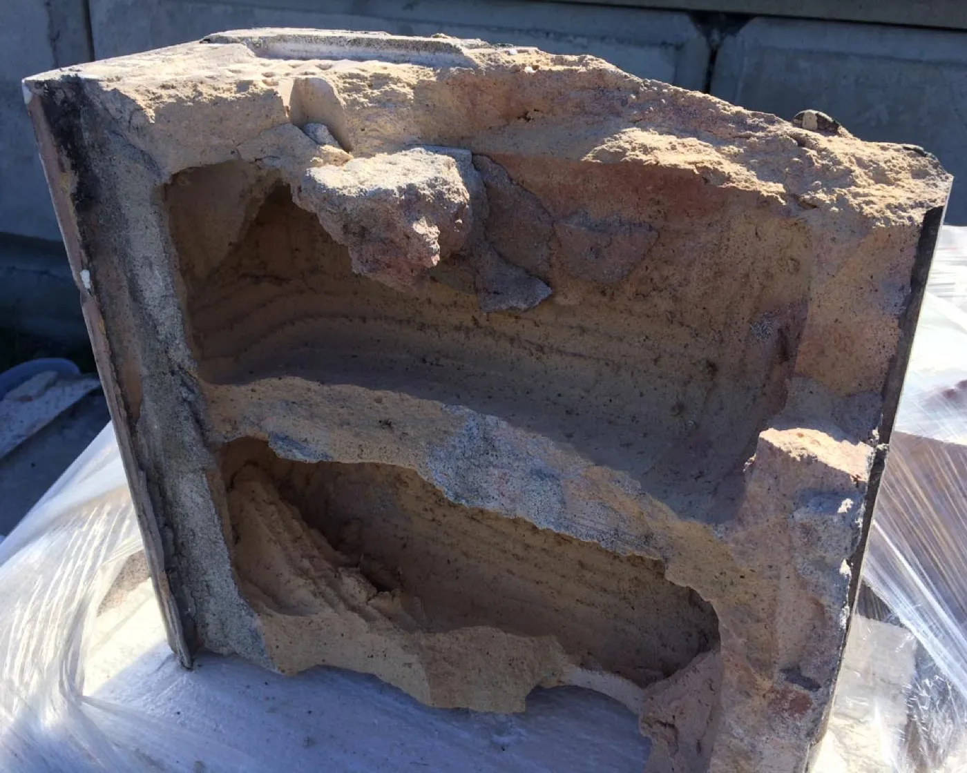 A broken original terracotta block, its hollow ribbed interior exposed where the face has sheared away