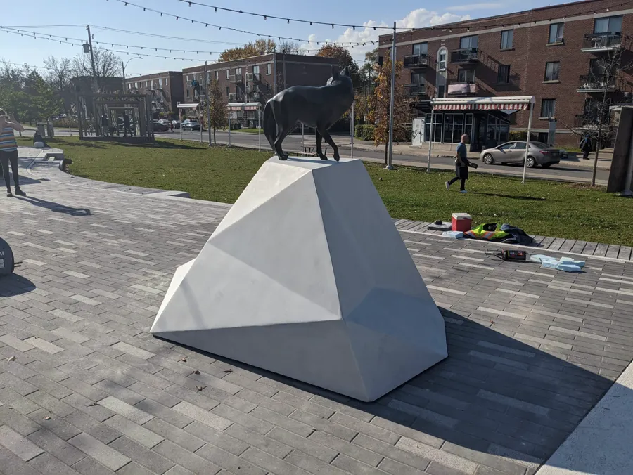 A faceted white UHPC plinth carrying a bronze animal sculpture in a paved public plaza